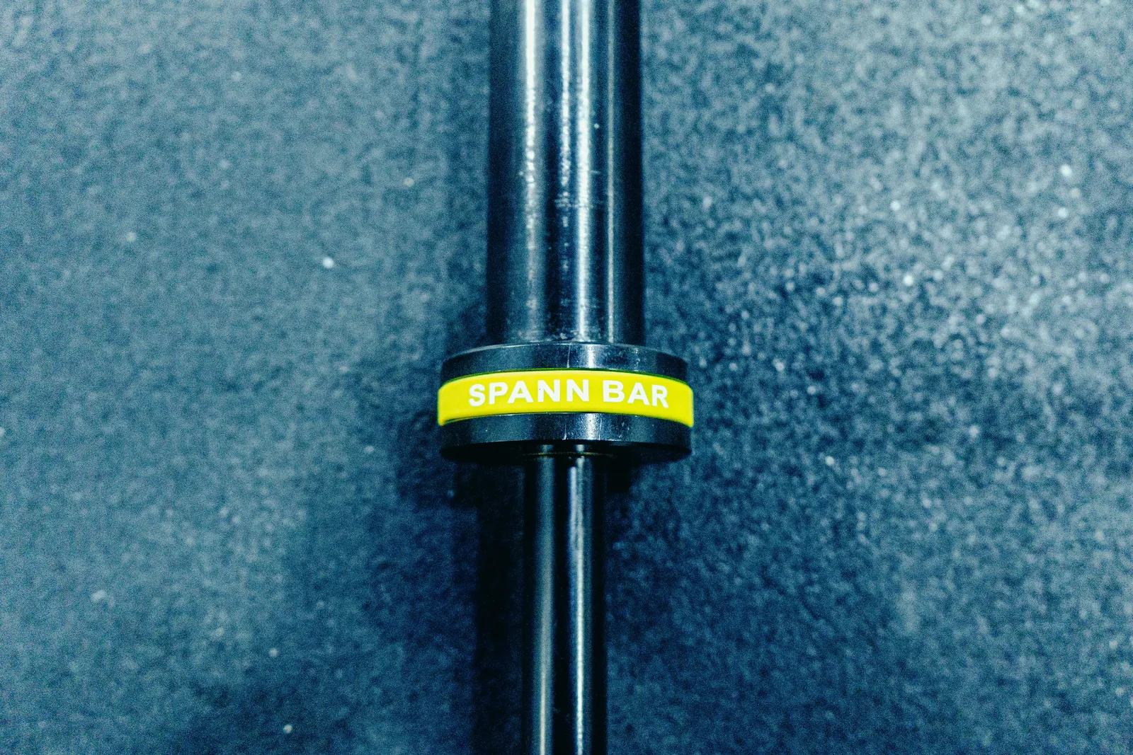 Macro of the Melo Bar's yellow Spann Bar collar on a rubber gym floor.