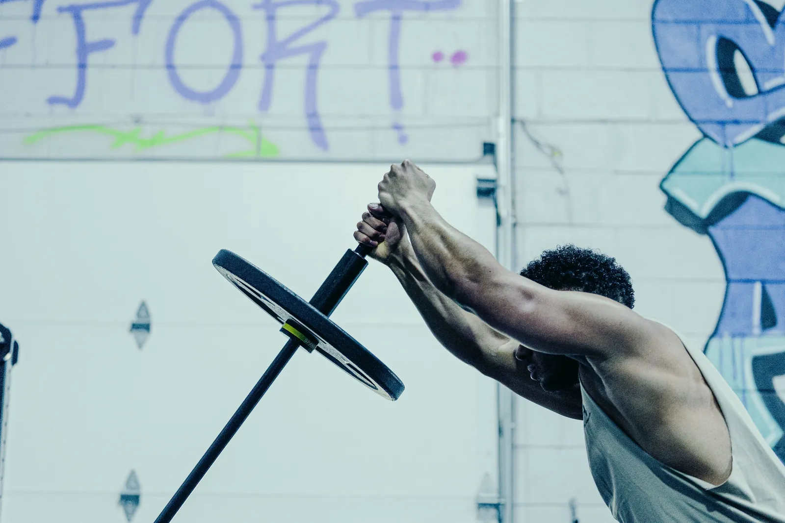 An athlete pressing the loaded Melo Bar overhead with both hands under the EFFORT wall.