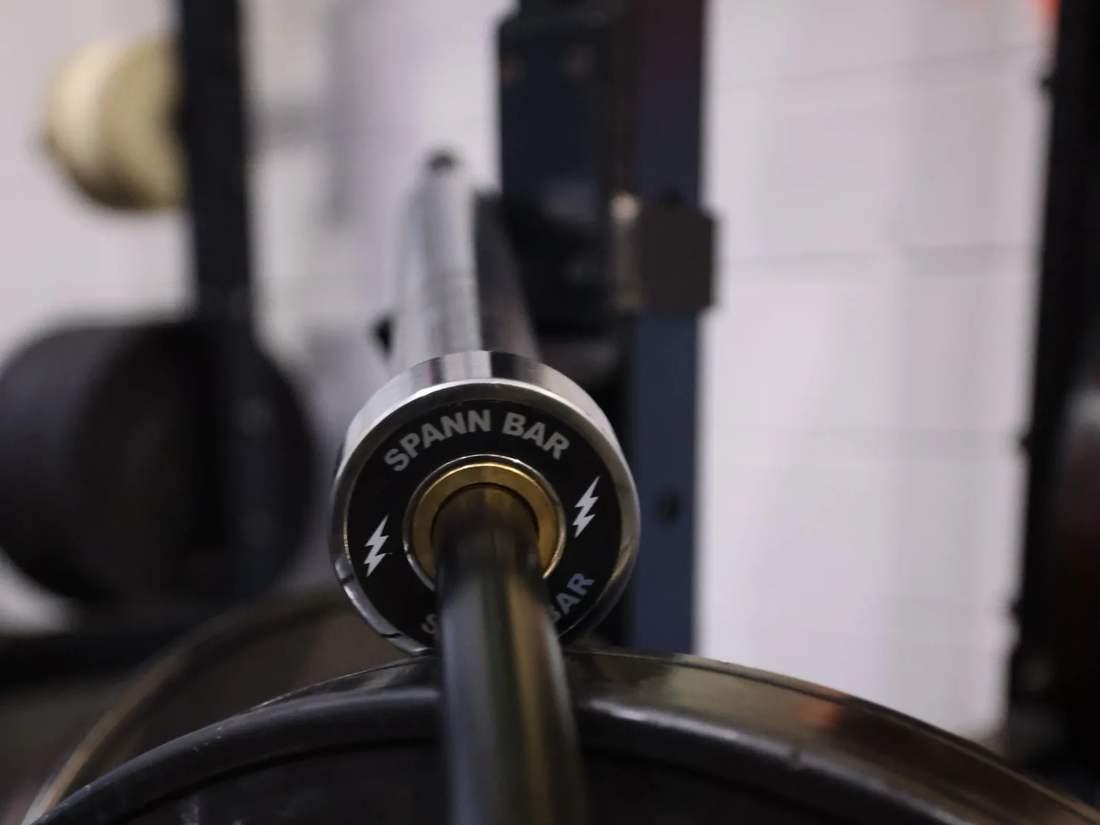 The Spann Bar end cap, silver lightning bolts, above a Rogue bumper plate in the rack.