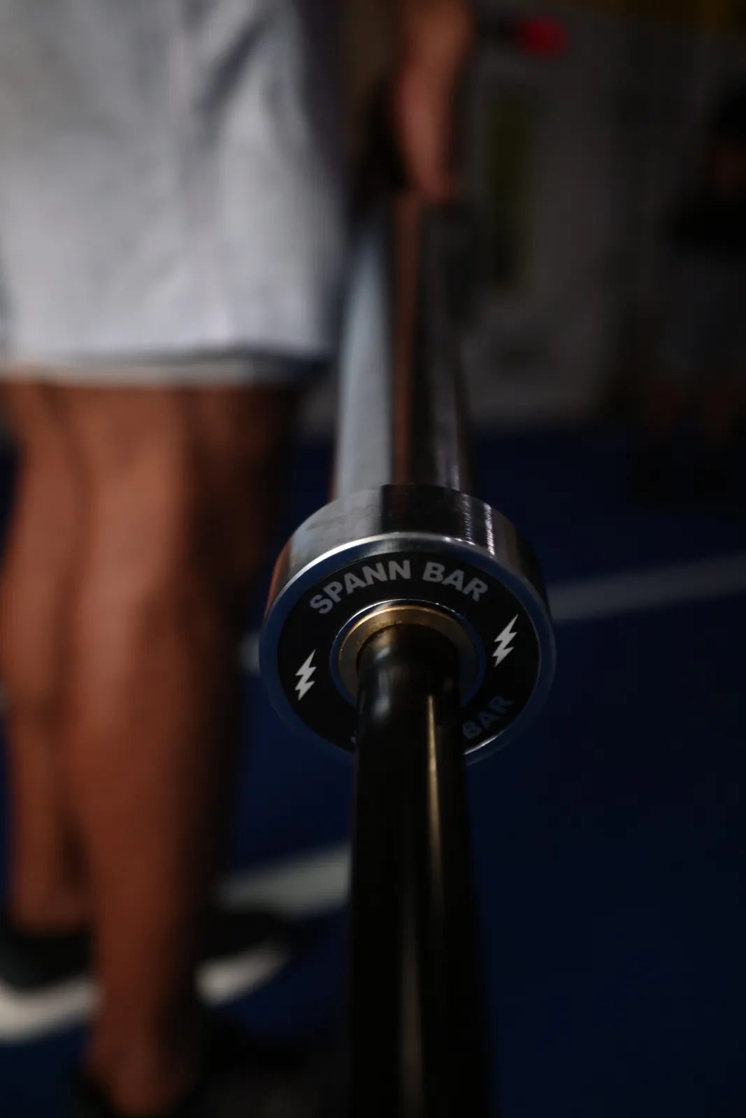 A hand on the loadable end of the Spann Bar, the silver-bolt cap toward the camera, on blue turf.