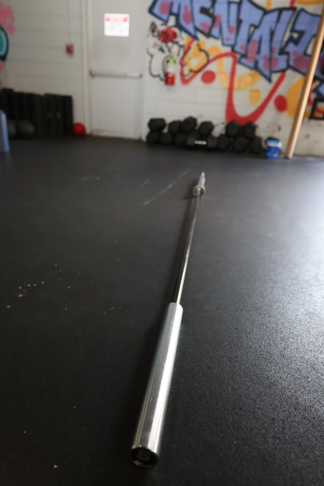 The whole Spann Bar on the gym floor from its landmine end, a graffiti wall behind it.