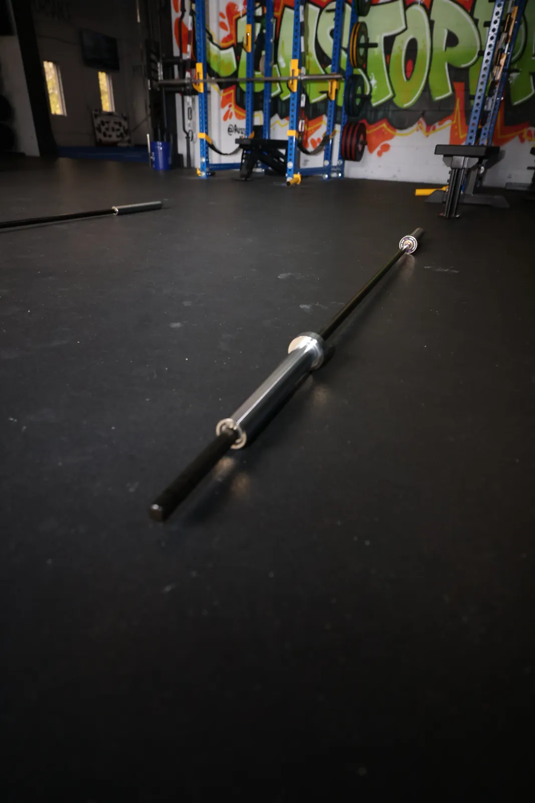 The whole Velencia Bar on the gym floor, knurled grip toward the camera, purple-bolt end cap at the far end.