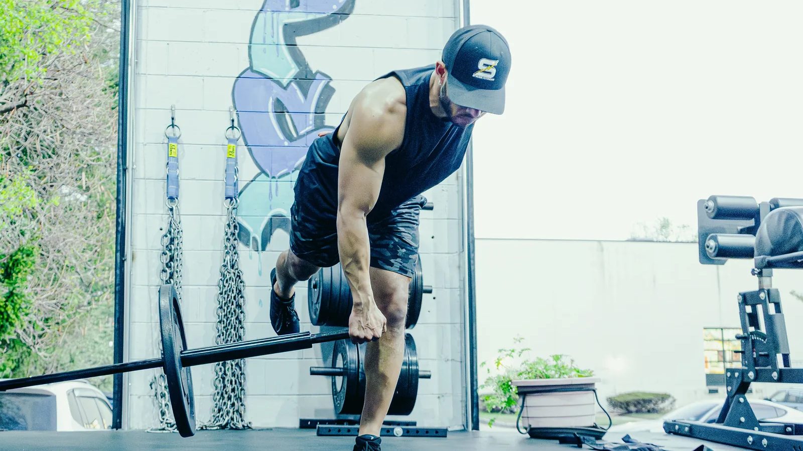 How to row with a landmine: a lifter hinged over the loaded end of a Spann Bar, pulling it to the hip in a single-arm landmine row at the open garage door